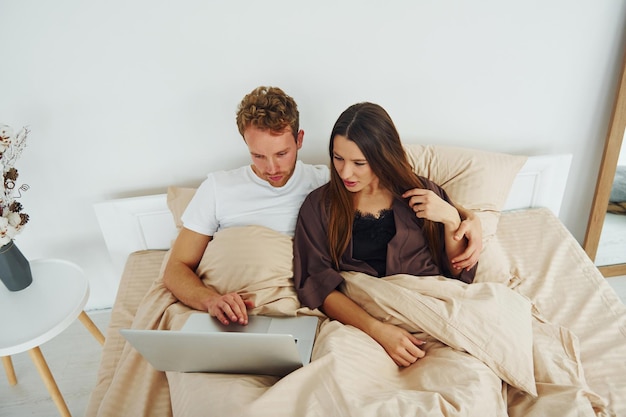 Couple lying down on bed with laptop Interior and design of beautiful modern bedroom at daytime