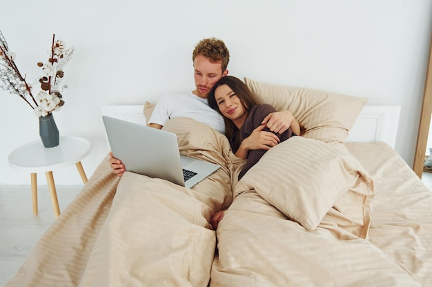 Couple lying down on bed with laptop Interior and design of beautiful modern bedroom at daytime