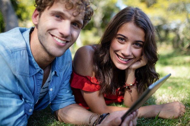 Couple lying on grass and using digital tablet