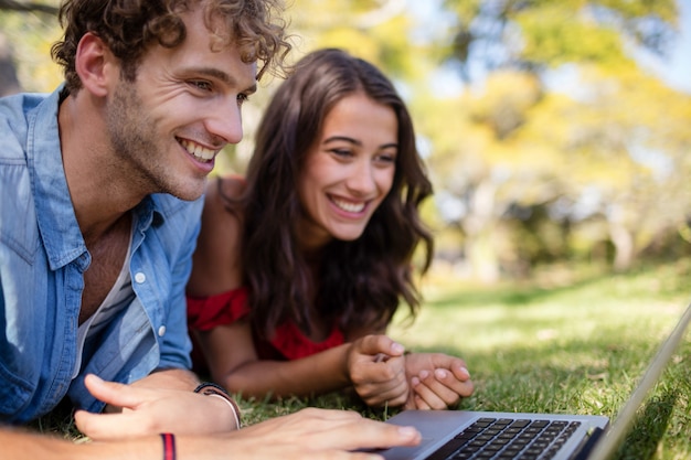 Couple lying on grass and using laptop