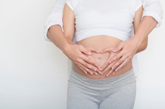 A couple making a heart shape on the pregnant belly with their hands isolated