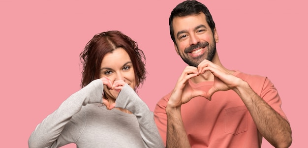 Couple making a heart with hands over isolated pink background