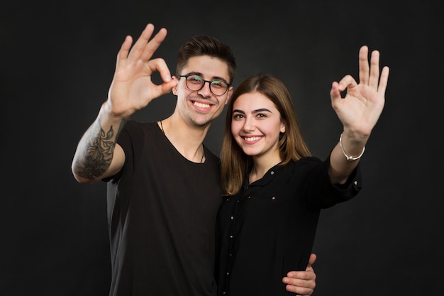 Couple making OK sign on black wall