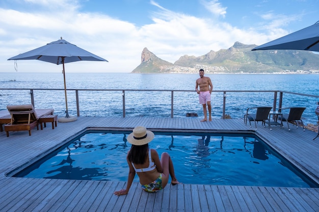 Couple man and woman in front of infinity pool looking out over\
the ocean of cape town south africa man and woman in swimming pool\
during sunset