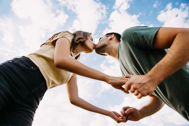 男性と女性のカップルが青い空の背景で手をつないでキスをしています