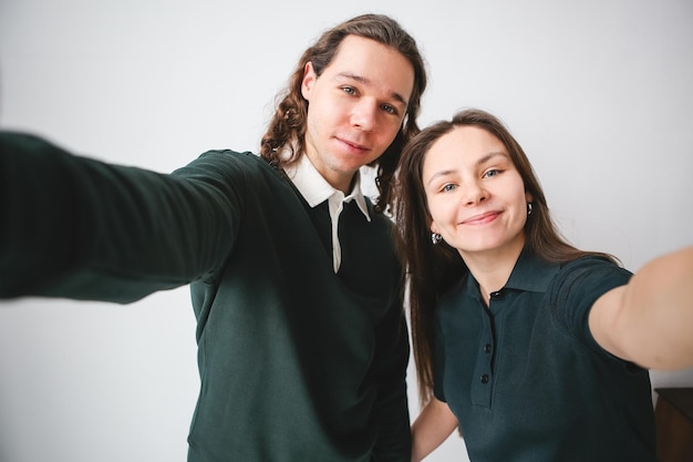 a couple man and woman hugging and taking a photo on the phone Couple taking selfie on white wall