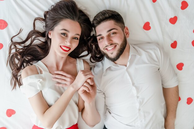 Couple man and woman in love on bed with red heart shapes at home