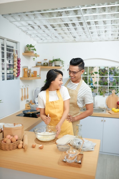 自宅のキッチンで自家製パスタを作りながらエプロンを着て楽しんでいるカップルの男女