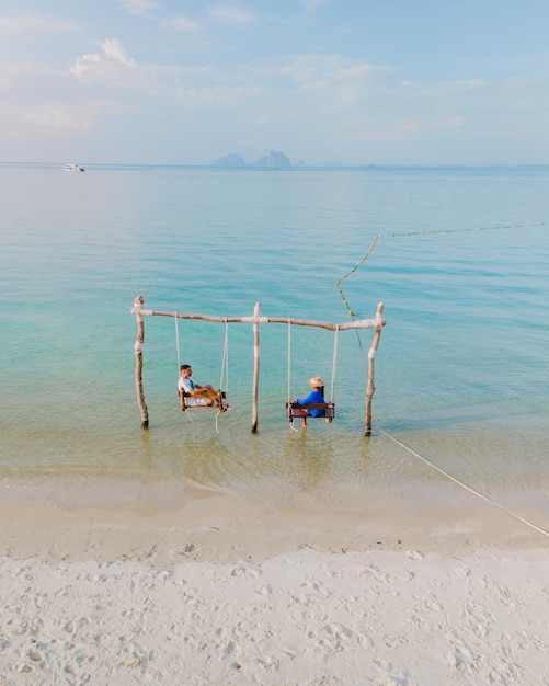 Photo a couple of men and woman on a swing at the beach of koh muk thailand