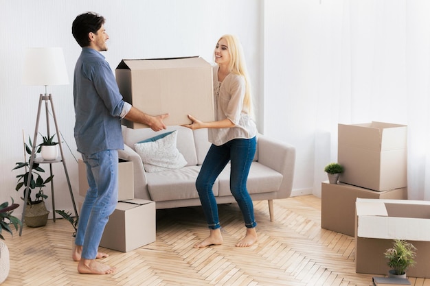 A couple moves a large cardboard box in a new apartment with bare feet and smiles