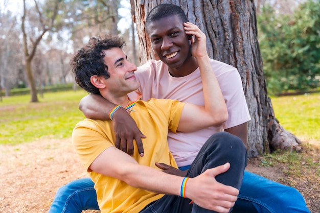 Coppia di uomini multietnici in un concetto lgbt del parco seduti accanto a un albero