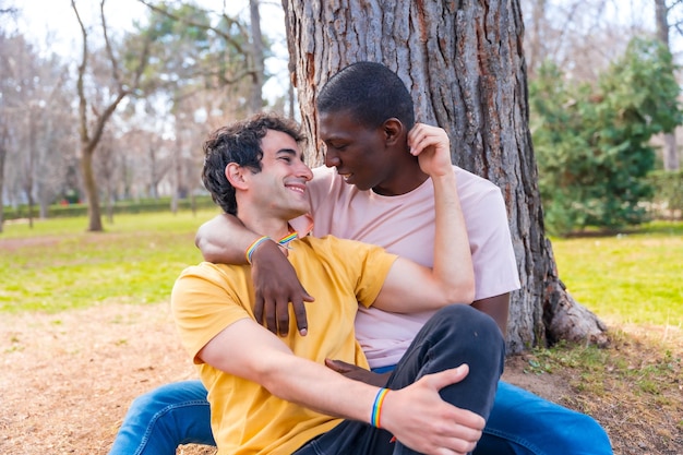 Couple of multiethnic men in a park lgbt concept sitting together a tree in a romantic pose