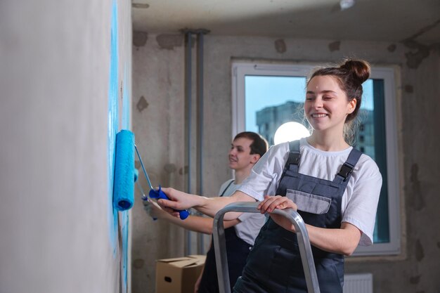 Couple in new home during repair works painting wall together happy family holding paint roller pain