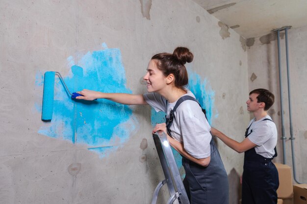 Couple in new home during repair works painting wall together Happy family holding paint roller painting wall with blue color paint in new house Home renovation DIY renew home concept