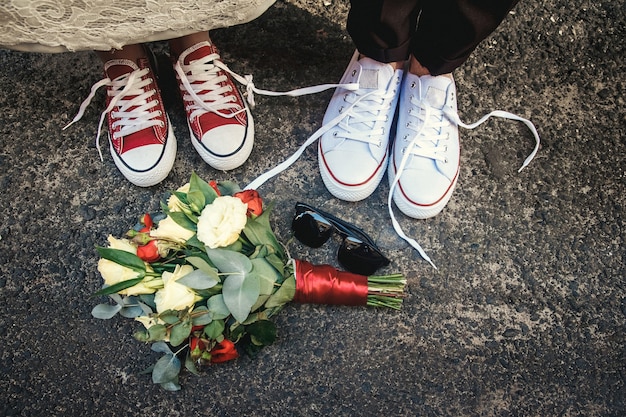 Couple of newly weddings with funny equal sneakers and wedding bouquet, sunglasses. Wedding details.