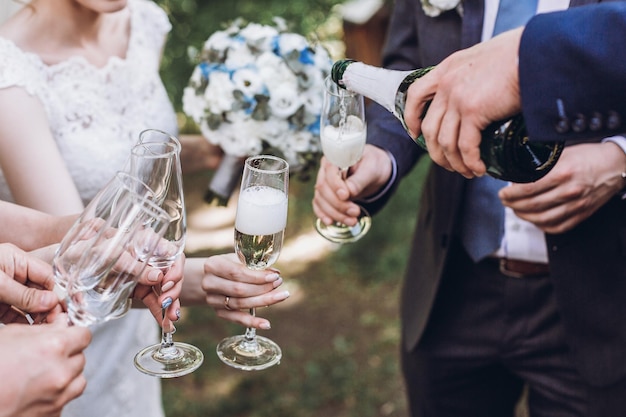 Foto coppia di sposi novelli sposi insieme a damigelle d'onore e groomsmen che bevono champagne all'aperto mani closeup celebrazione del matrimonio con gli amici