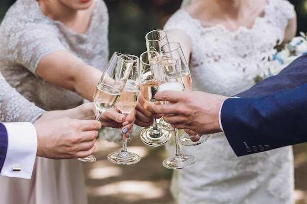 Couple of newlyweds bride and groom together with bridesmaids and groomsmen drinking champagne outdoors hands closeup wedding celebration with friends