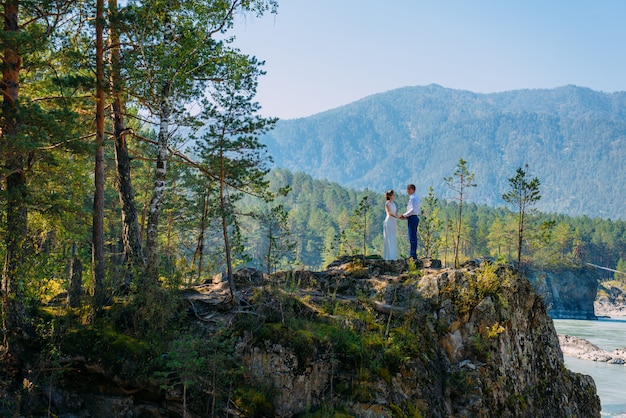 A couple of newlyweds stand in the wild nature and gaze at each other