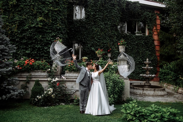 ツタと家の庭で結婚式の日に傘の下でキスする新婚新郎と新婦のカップル