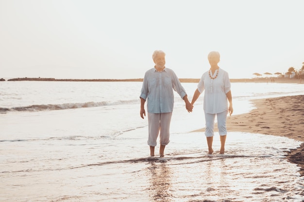 노년 부부가 함께 모래 위를 걷고 해변의 모래 위에서 신나게 노는 순간을 즐기며 생활 신나게 즐기는 사랑에 빠진 귀여운 두 선배 맨발로 물 위를 걷는 Xa