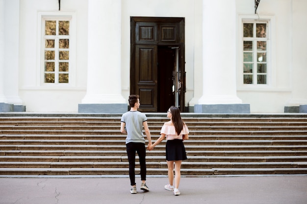 Пара влюбленных студентов уверенно идет в обычный университет, держа друг друга за руку, готовясь к новому дню обучения