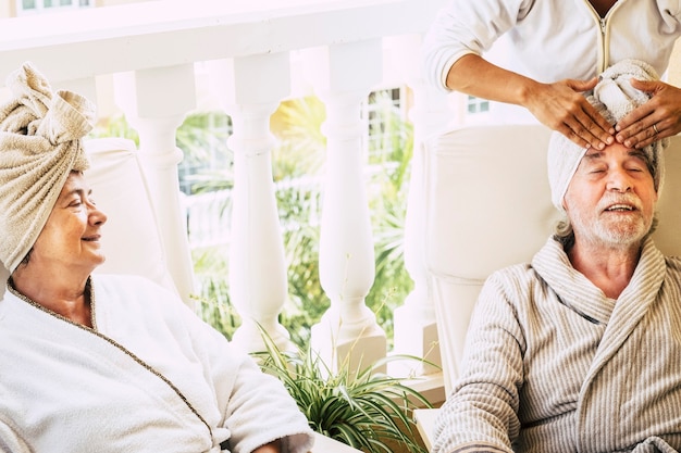 Фото Пара из двух пенсионеров на курорте, делающая косметические процедуры вместе с помощью женщины, делающей массаж мужчине - зрелые люди в отеле расслабились