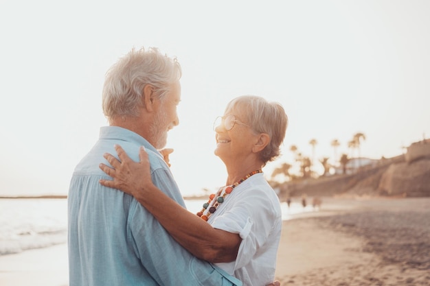 Couple of old mature people dancing together and having fun on the sand at the beach enjoying and living the moment Portrait of seniors in love looking each others having fun