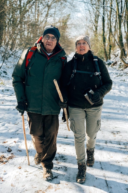 Couple older people enjoy the outdoor activity winter walking in the snowy wood birdwatching and trekking