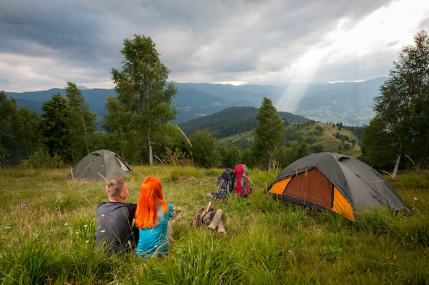 Фото Пара на зеленой траве возле костра, палатки, рюкзаки