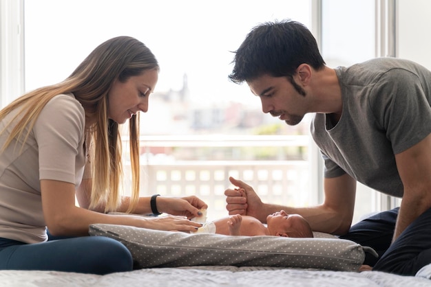 A couple of parents changing the diapers to their newborn son on the bed