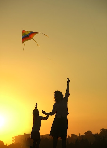 a couple of people are flying a kite with the sun behind them