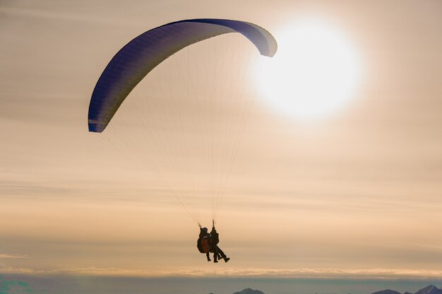 Couple of people flying on a parachute with big shining sky