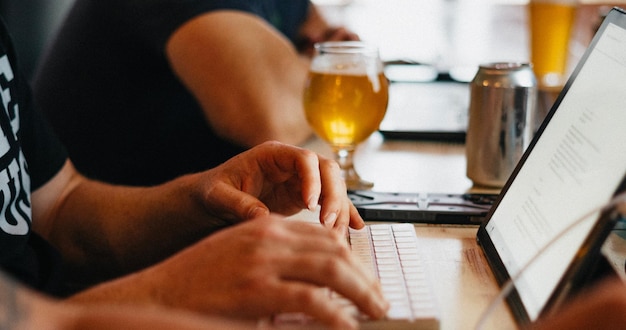 a couple of people typing on their laptops with a glass of beer in the background