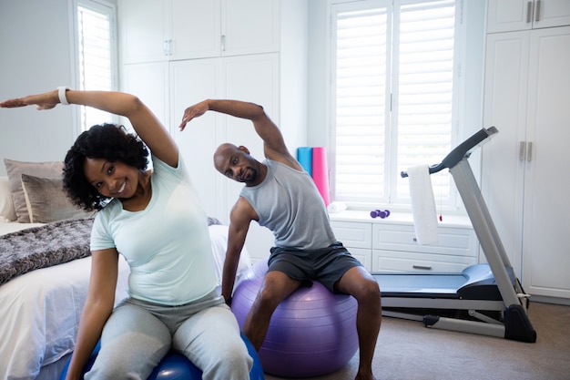 Пара выполняет упражнения на растяжку на фитнес-мяч в спальне