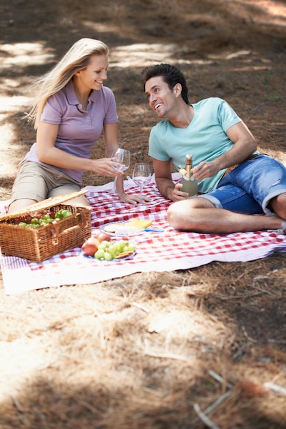 Couple picnic and champagne in forest with love romantic celebration and summer date on valentines day Young people with food fruits and bottle with wine glasses in woods or nature on anniversary