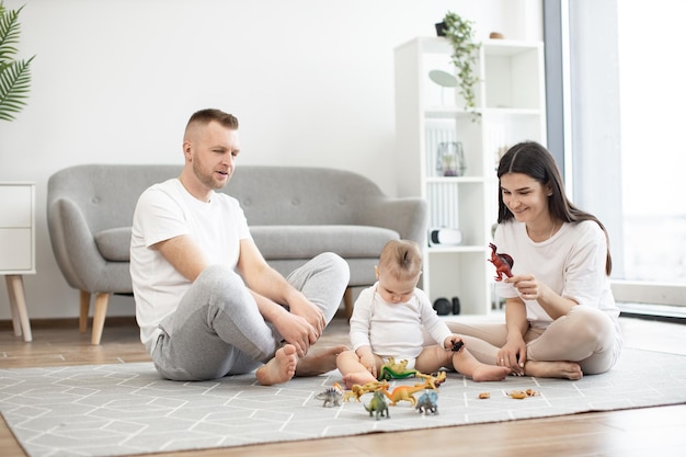 Couple playing dinosaur game with infant on carpet at home