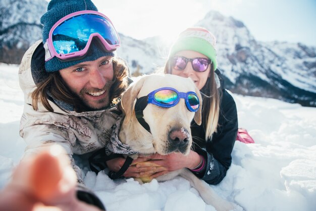 雪に覆われた地面に山で犬と遊ぶカップル