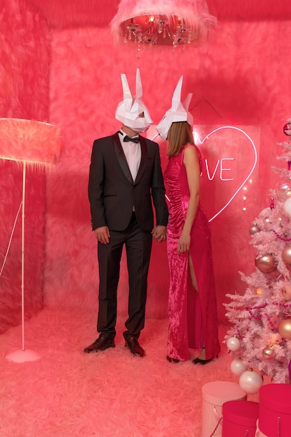 The couple in poligonal rabbit masks closeup on the pink background are celebrating New 2023 year. C