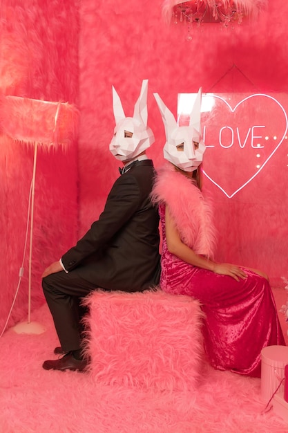 The couple in poligonal rabbit masks closeup on the pink background are celebrating New 2023 year. C