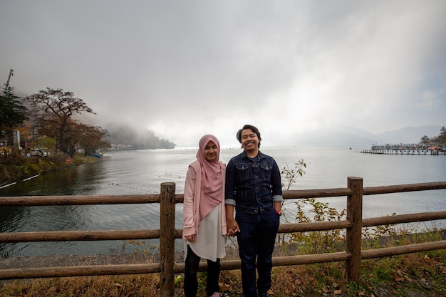 A couple poses in front of a lake with a cloudy sky in the background.