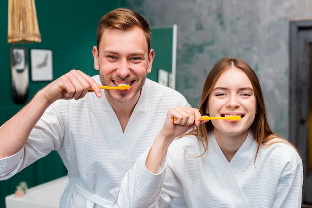 Couple posing in bathrobes while brushing their teeth