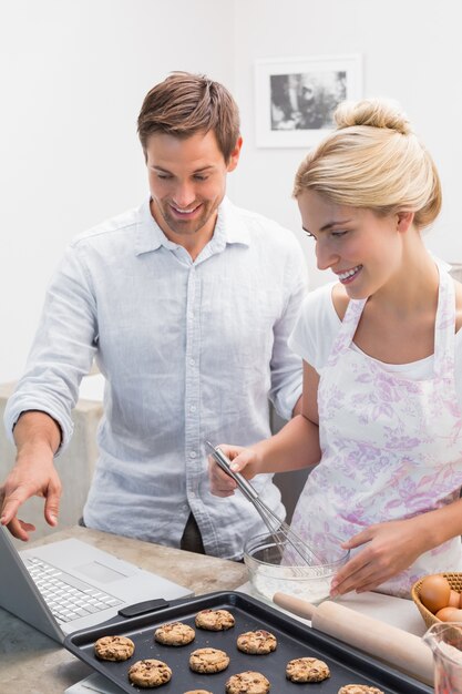 Couple preparing cookies while using laptop in the kitchen