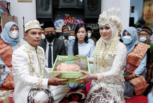 A couple presents a box of chicken to a couple at a wedding.