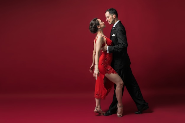 Couple of professional tango dancers in elegant suit and dress\
pose in a dance move on red background