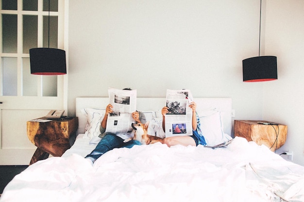couple reading newspaper while sitting on bed at home