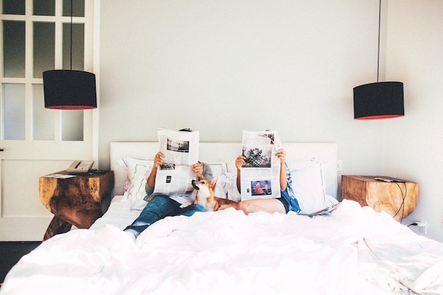 Photo couple reading newspaper while sitting on bed at home