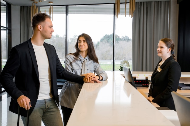 Couple and receptionist at counter in hotel. Young couple on a business trip doing check-in at the hotel