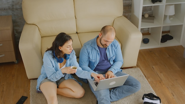 Couple relaxing on floor browsing on internet after furniture.