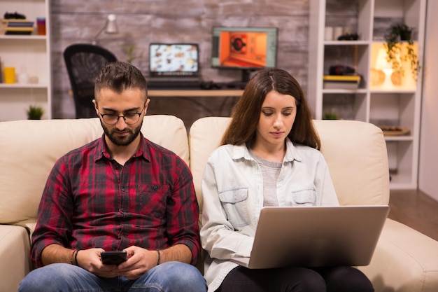 Couple relaxing on sofa using their phone and laptop for online shopping.