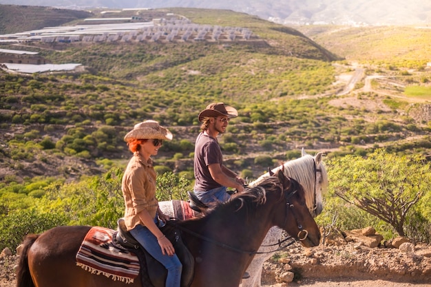 Coppia di cavalieri uomo e donna con cavalli marroni e bianchi vanno a godersi l'attività di svago all'aperto in escursione in viaggio per le montagne. cowboy moderno e nessuna tecnologia